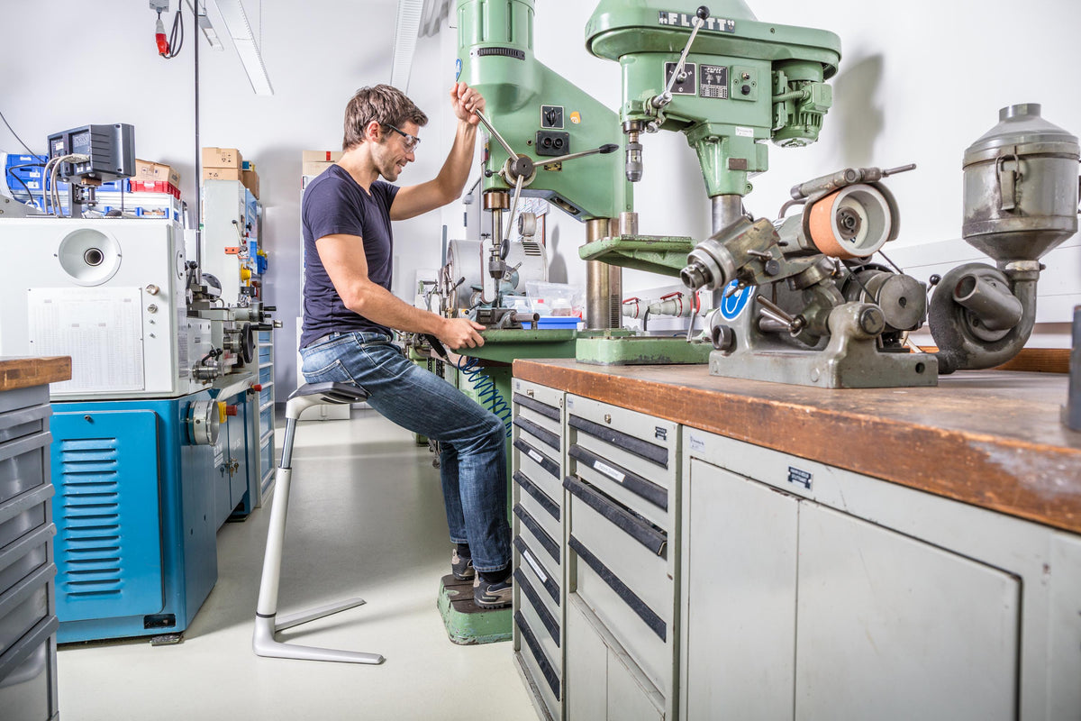 Worker in a machine shop leaning on an ESD protected FIN chair at a workbench
