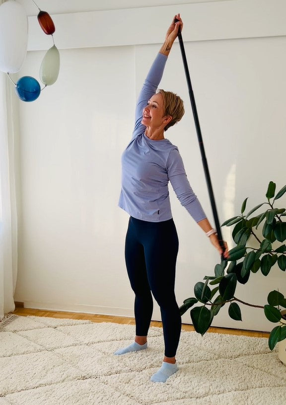 Woman exercising with a long bar held overhead indoors