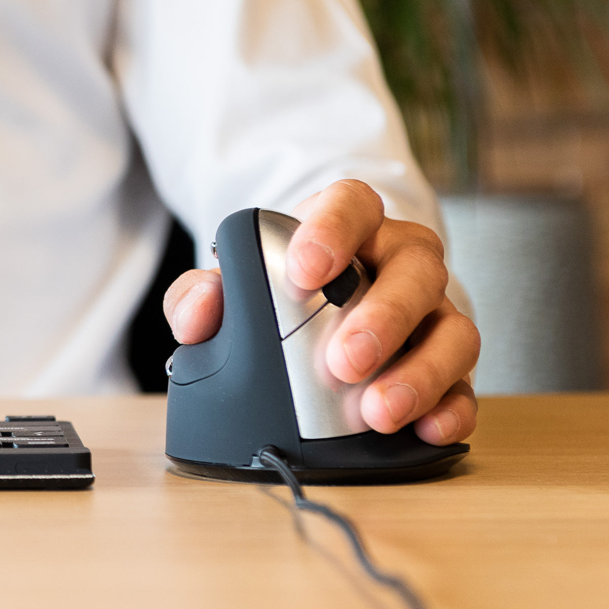 Hand using an HE Mouse left-handed vertical mouse beside a keyboard