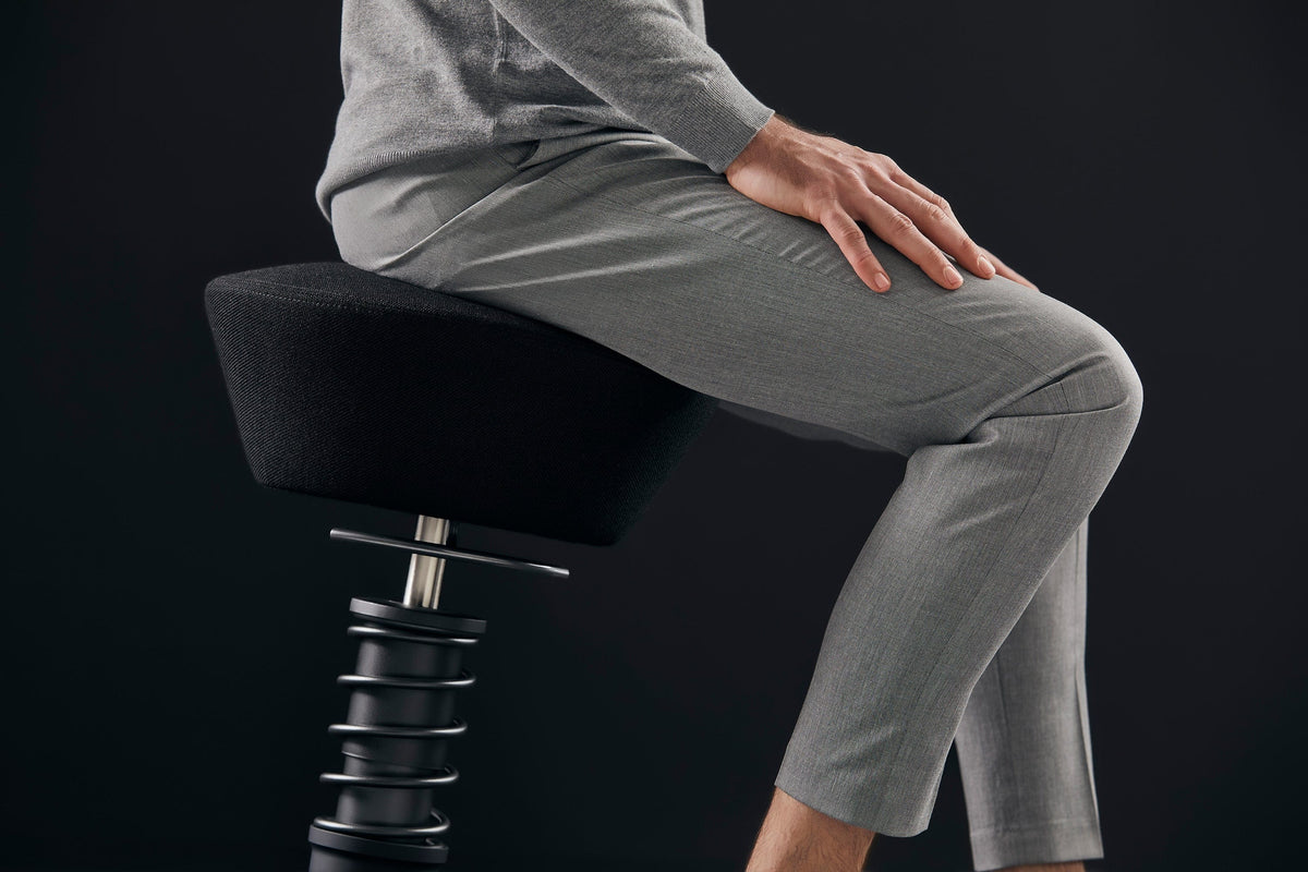 Person seated on a red Swopper active chair, viewed from the side against a dark background