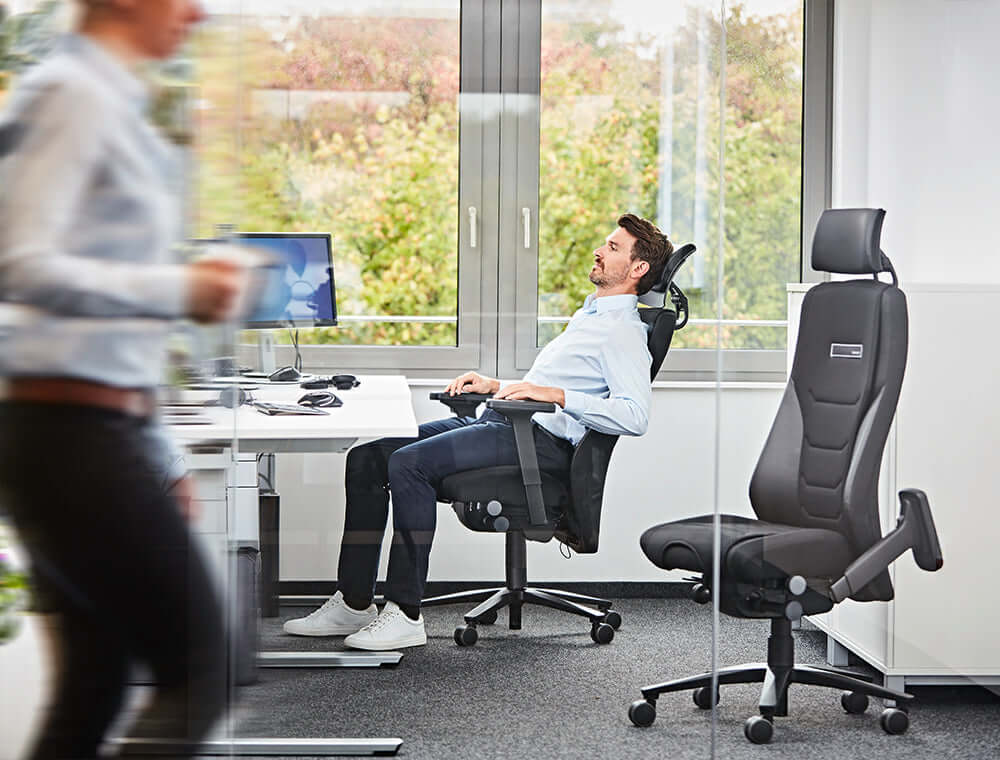Man sitting on TWENTYFOURis5 control room chair, demonstrating ergonomic features and adjustable headrest, ideal for office use.