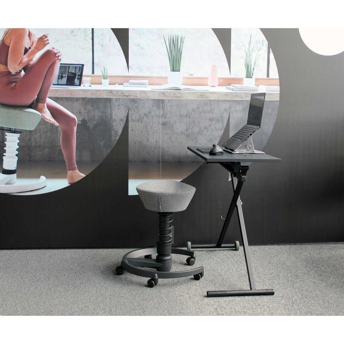 Adjustable black GetUpDesk Move with foldable design and wheels, shown in a modern interior workspace with a computer setup.