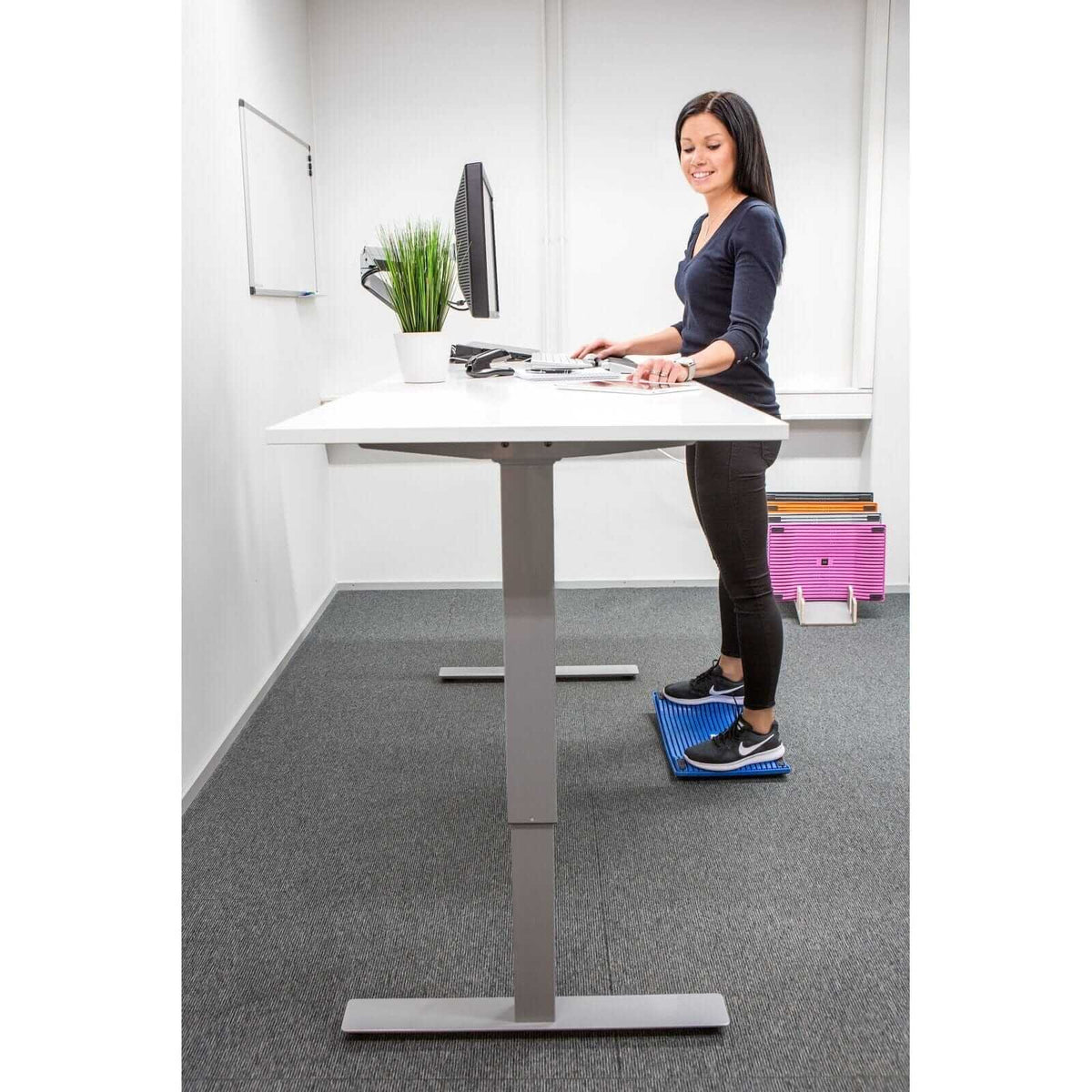 Woman using Gymba activation board at standing desk to improve health and productivity in office setting.