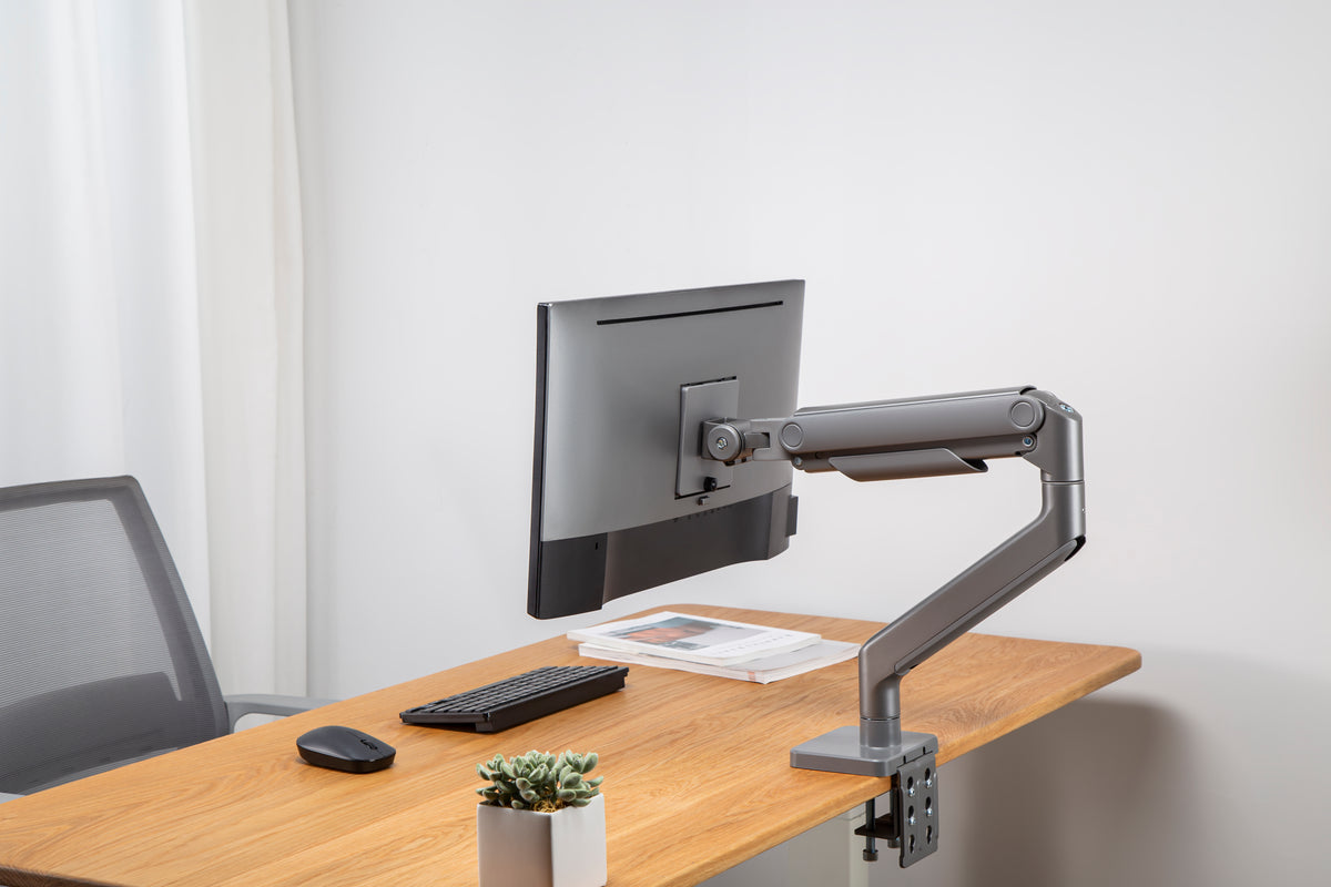 Wooden desk with a monitor on a heavy duty arm, keyboard and mouse