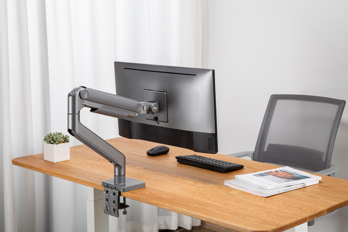 Wooden desk with a monitor on a heavy duty arm beside an open laptop