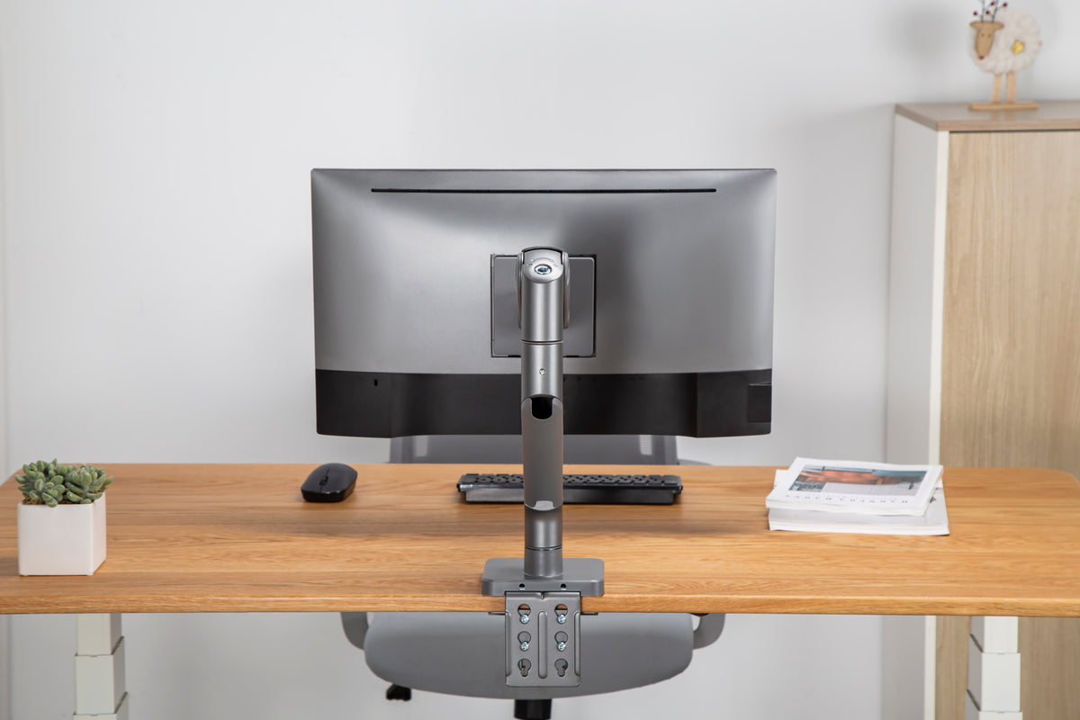 Monitor mounted on a heavy duty arm above a wooden desk, seen from the front