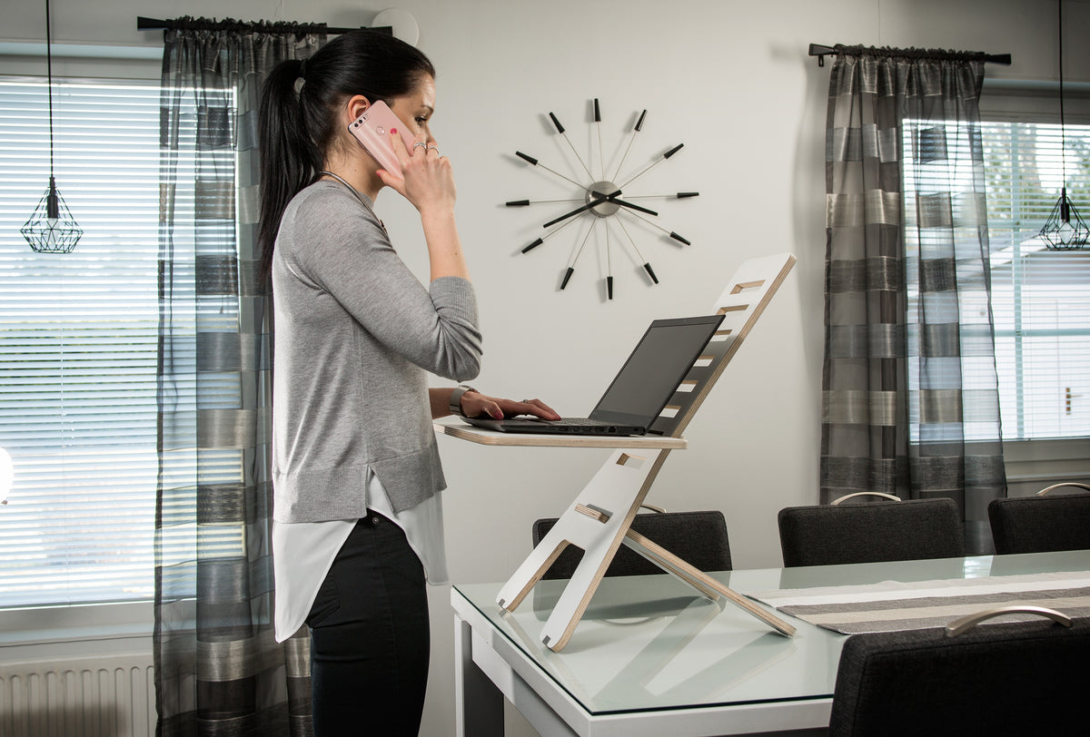 Woman working at a GetUpDesk Light standing laptop stand beside a window