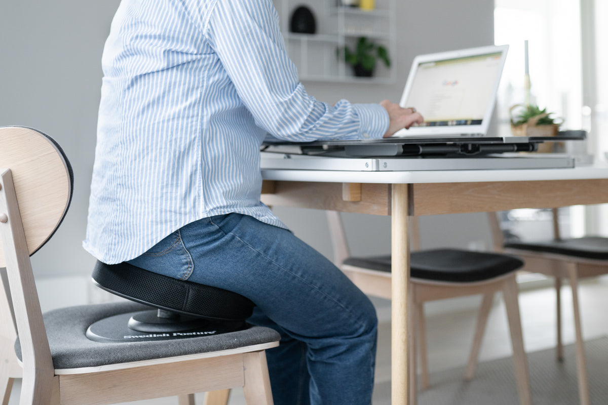 Man working at a desk while seated on a posture balance active seat