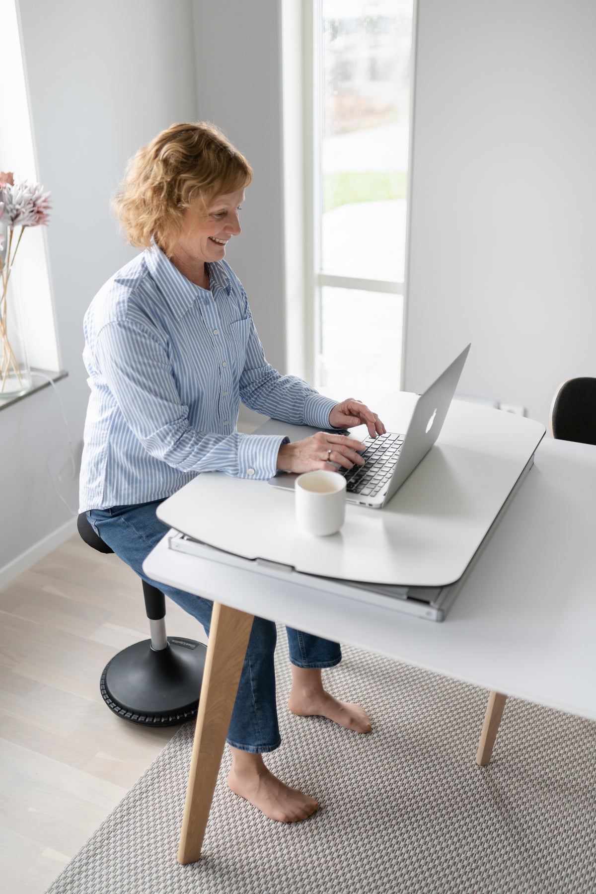 Woman working at a lowered GetUpDesk Free tabletop in a bright room