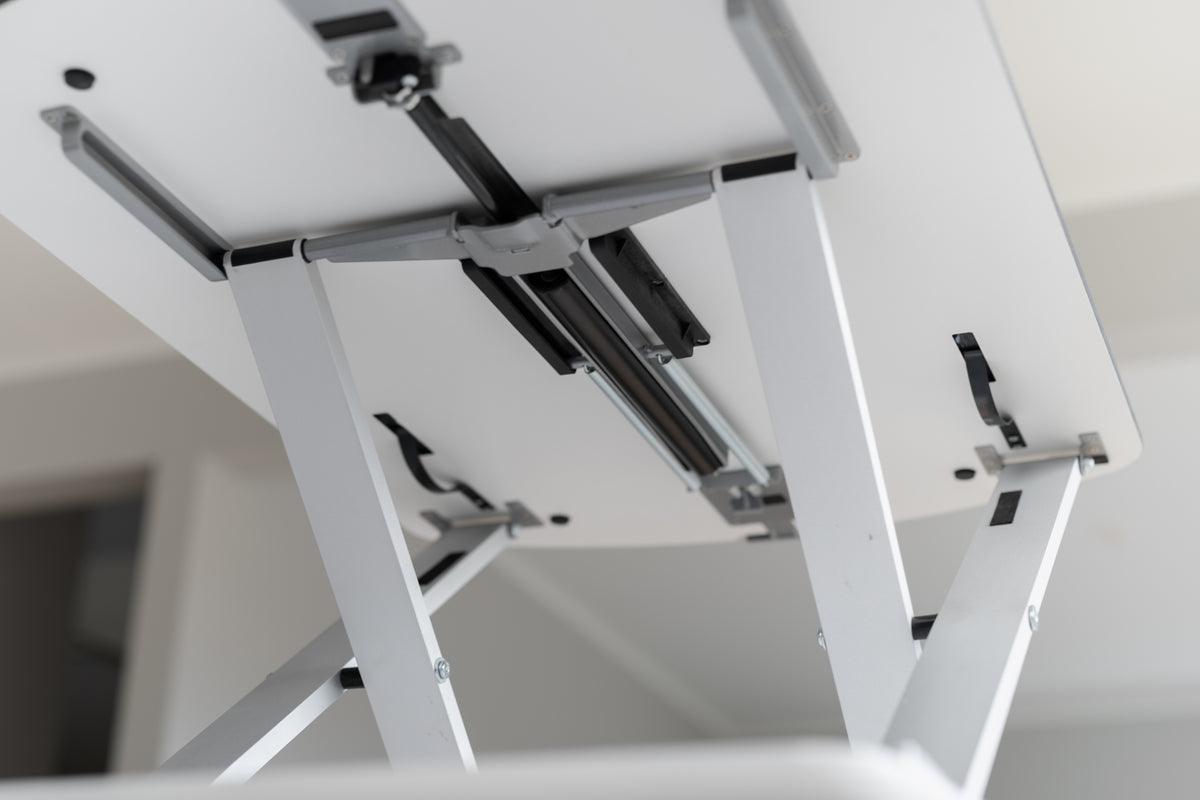 Detail of the white scissor frame and gas lift under the GetUpDesk Free tabletop