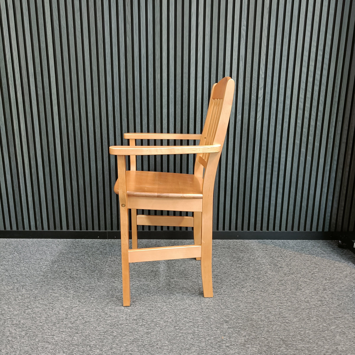 Petteri elevated wooden chair in beech with armrests and a slatted back, seen at an angle