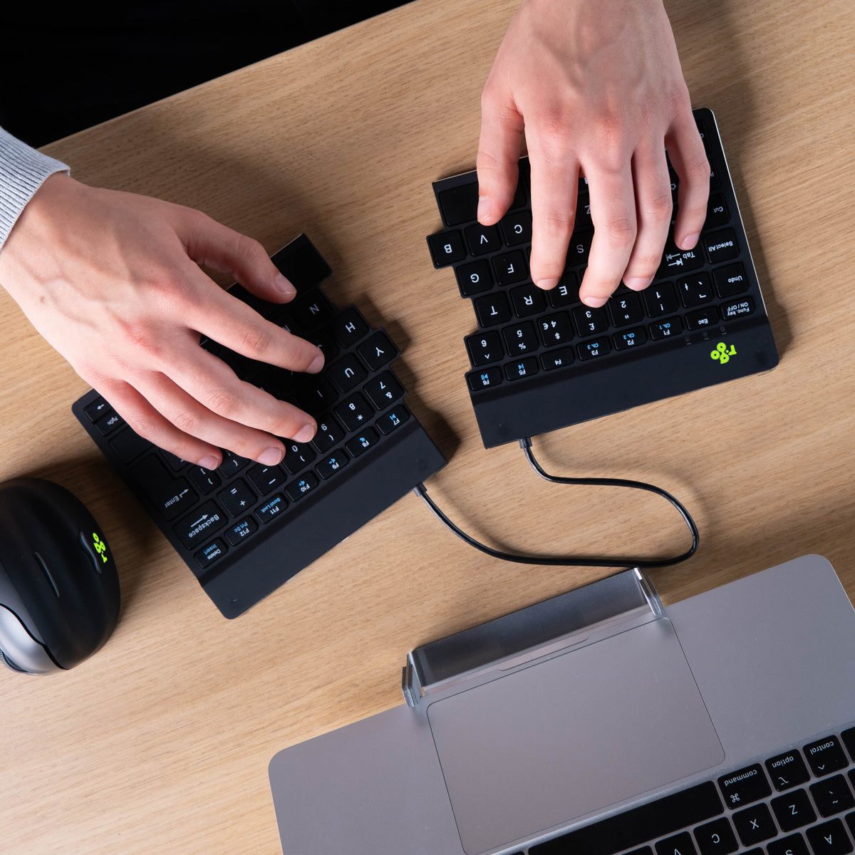 Hands using an Ergo-R split keyboard and mouse on a grey desk surface