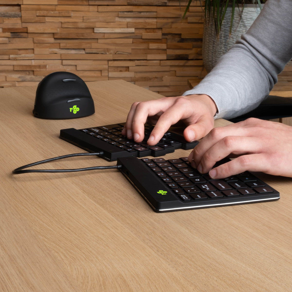 Person typing on an Ergo-R split keyboard at a wooden desk with a vertical mouse