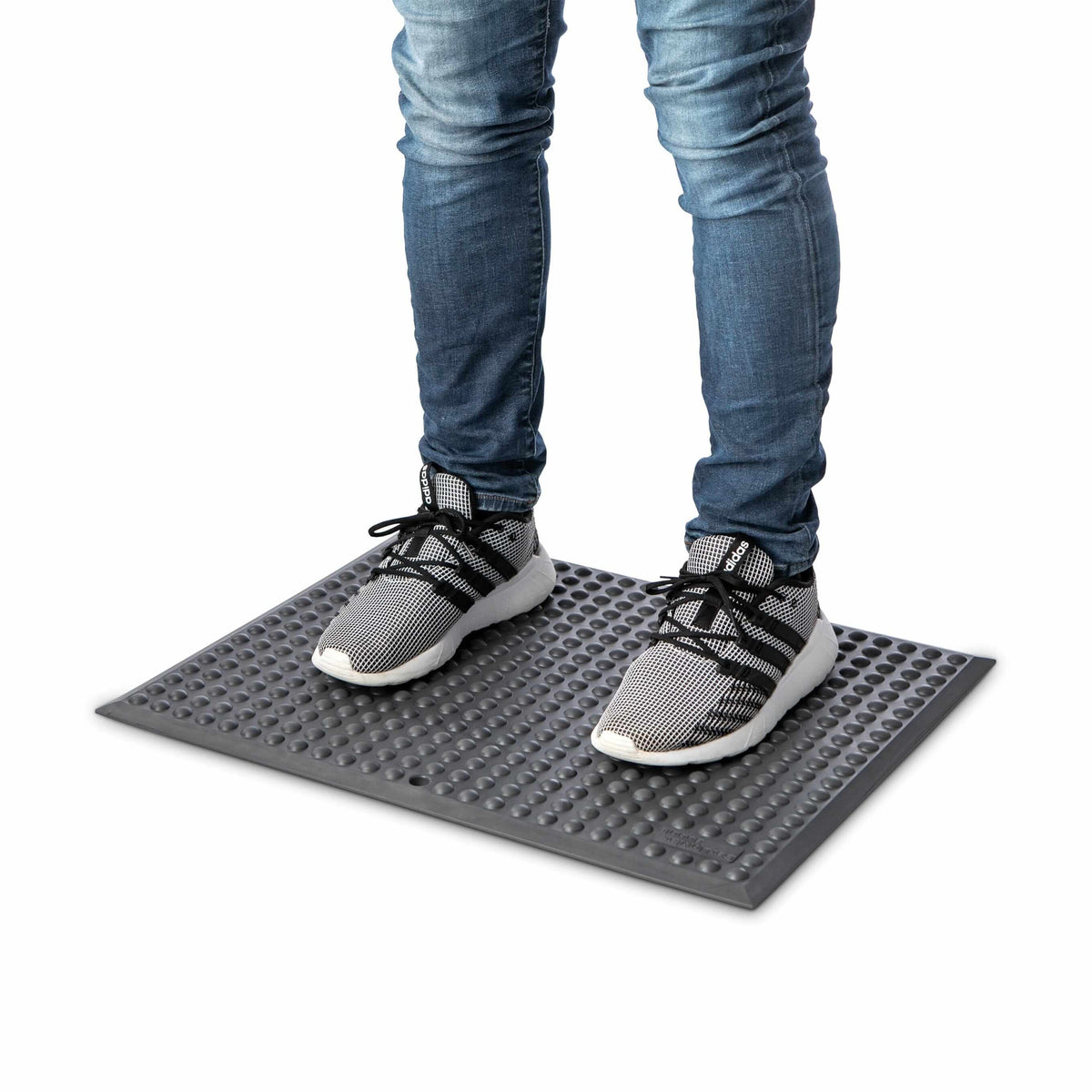Person standing on GetUpMat Bubble workstation mat, dark grey, designed to reduce fatigue and improve circulation during standing tasks.