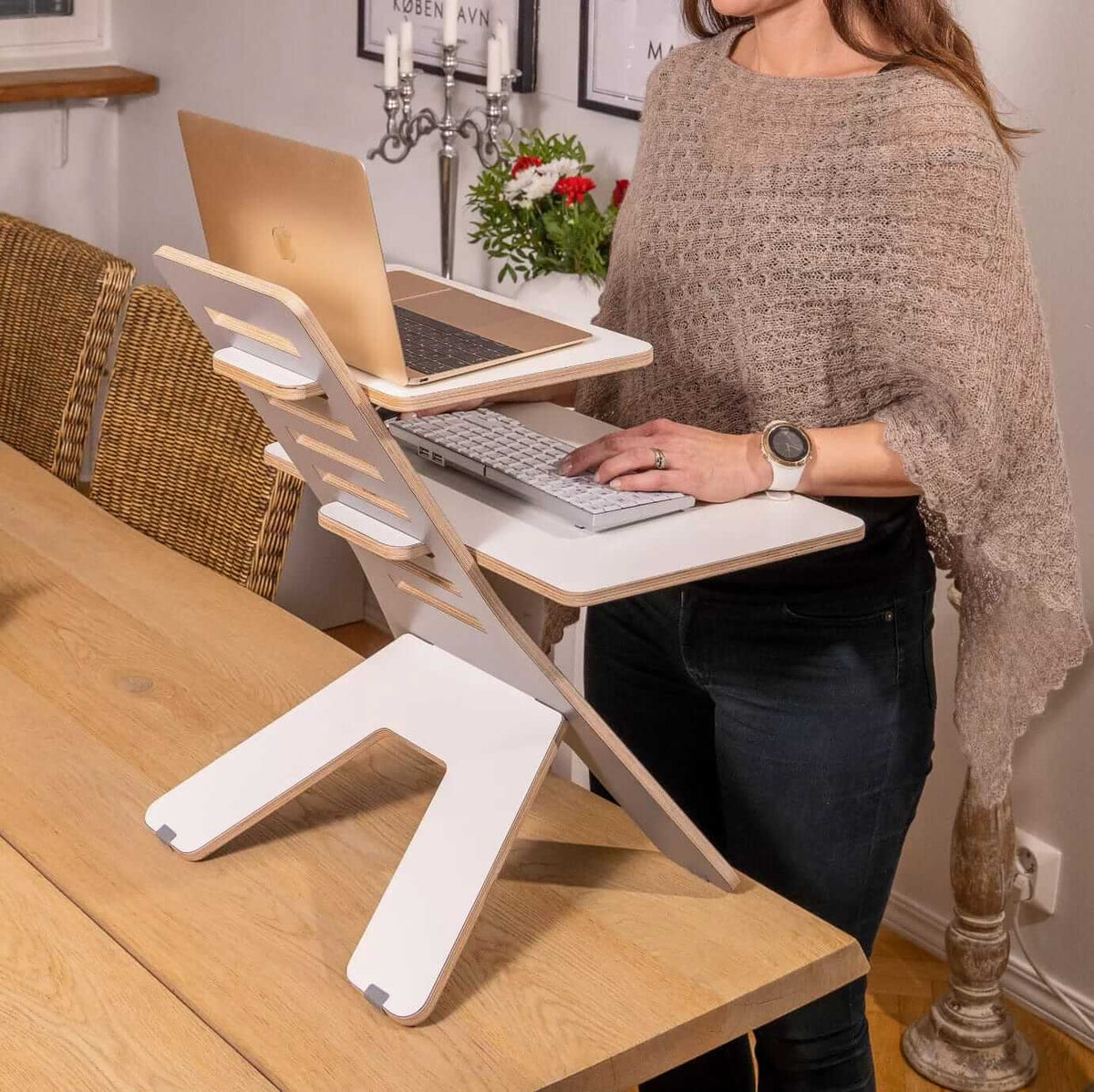 Woman using GetUpDesk Light laptop stand with additional shelf for ergonomic workspace.