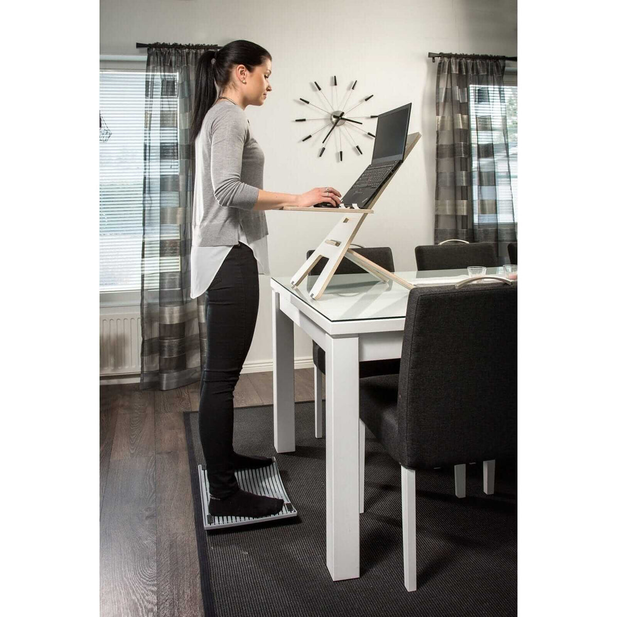 Woman using Gymba activation board at standing desk for improved concentration and circulation in modern office setting.