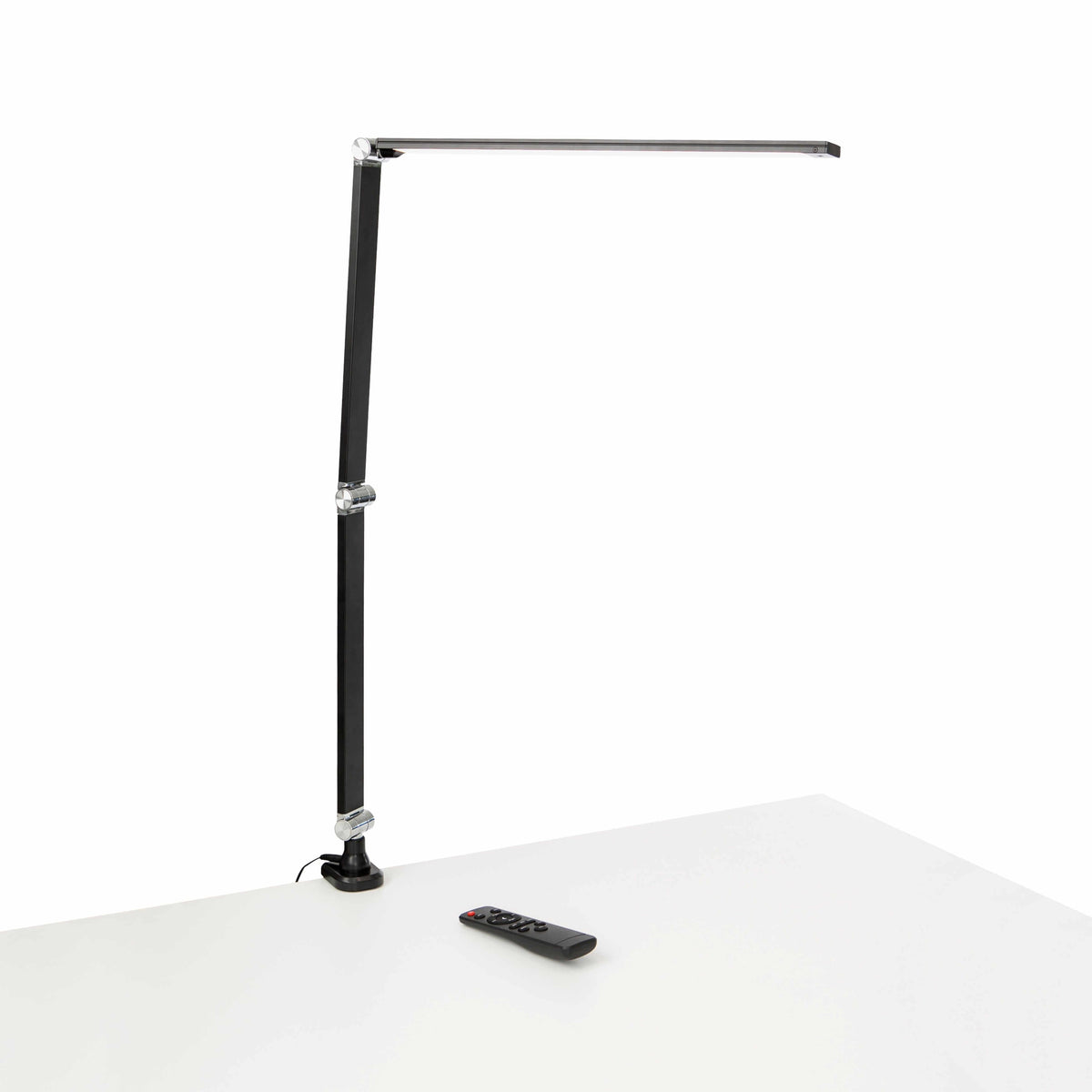 Musta Link LED -työpistevalaisin ja kaukosäädin valkoisella pöydällä.